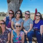 six women sitting on a picnic bench in a paso robles vineyard on a wine tour