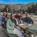 3 women and 3 men sitting at a picnic bench in a park under a blue sky in winter in Paso Robles, CA