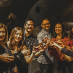 a large group cheersing with glasses of wine in a wine cave
