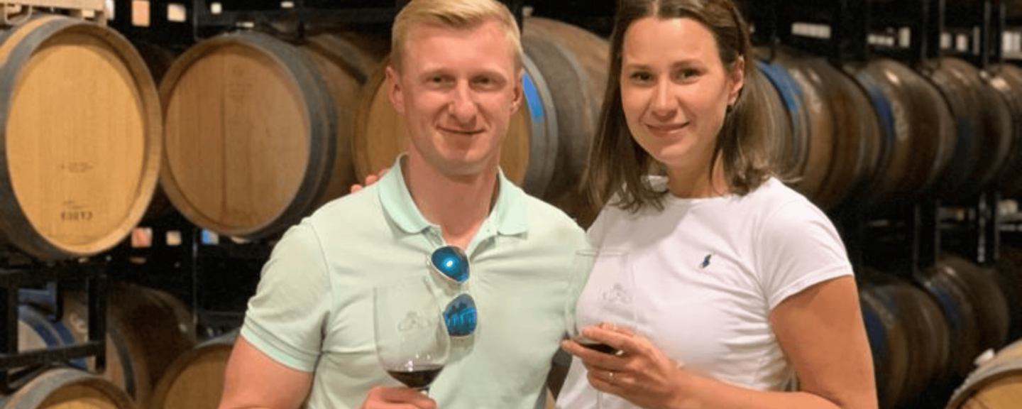 a couple drinking a popular red wine in a room with wine barrels from floor to ceiling