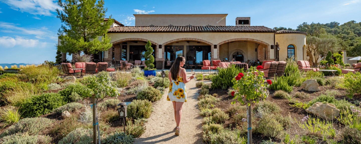 a woman walking down a pathway drinking a glass of wine at a paso winery
